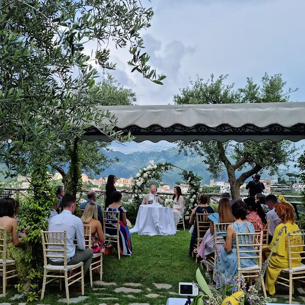 Outdoor clifftop ceremony with guests seated under olive trees overlooking a mountain village