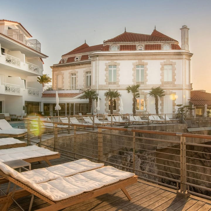 Sun loungers on a coastal terrace beside a historic white hotel at golden hour