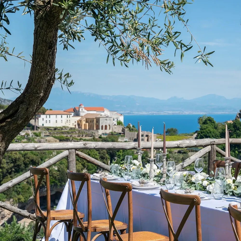 Outdoor wedding table set with white florals and candles overlooking a coastal bay and mountains