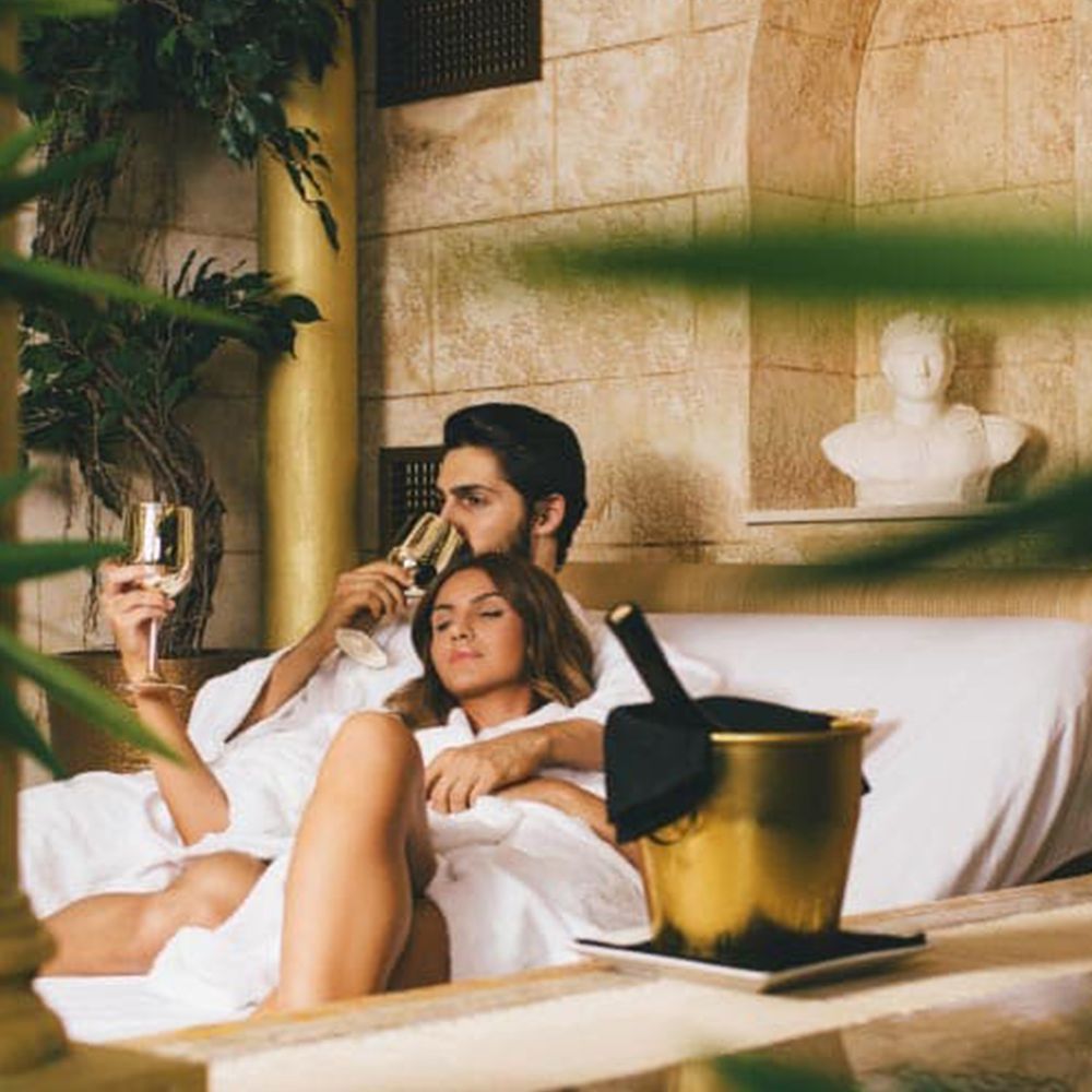 Couple in white robes relaxing with champagne beside a poolside spa cabana