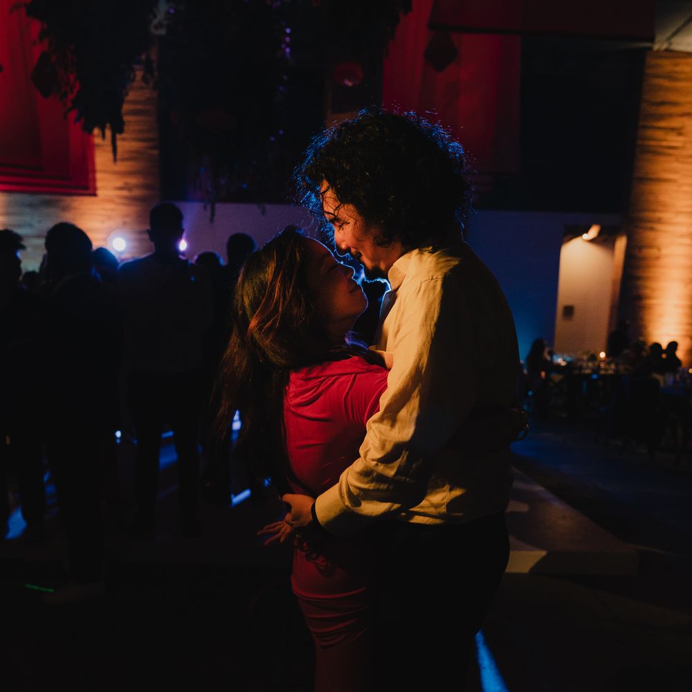 Two people embracing on a dimly lit dance floor beneath hanging dried florals