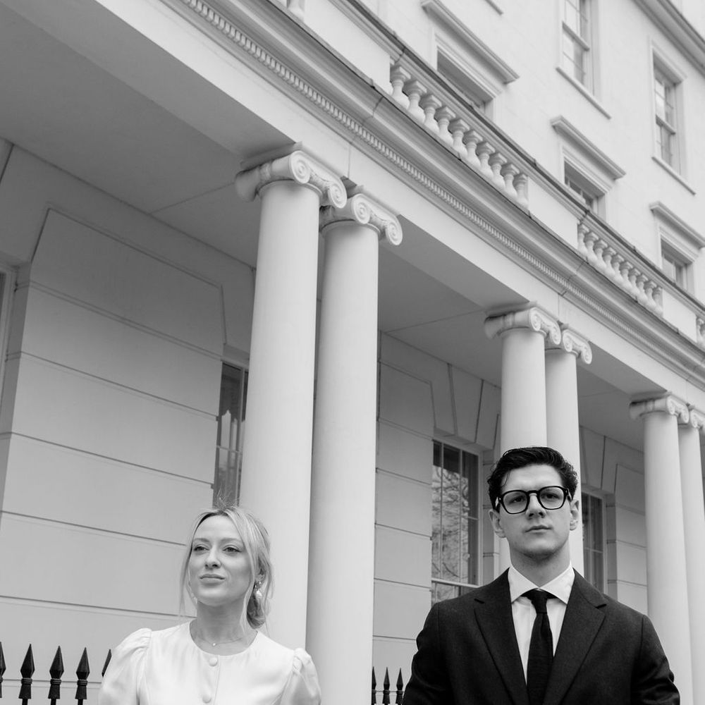 Bride and groom holding hands outside a grand columned townhouse in black and white