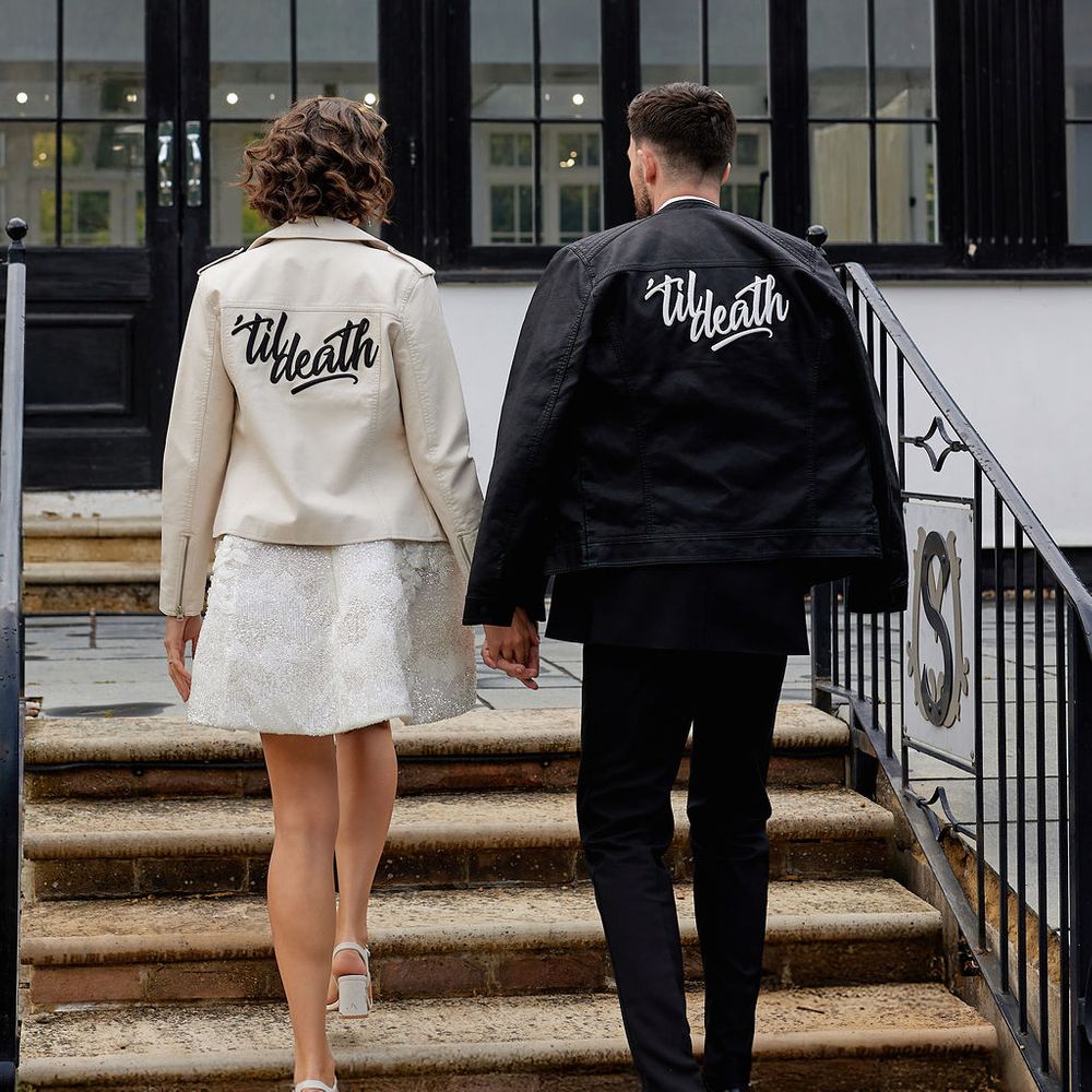 Couple hold hands walking upstairs in matching leather jackets with 'til death lettering