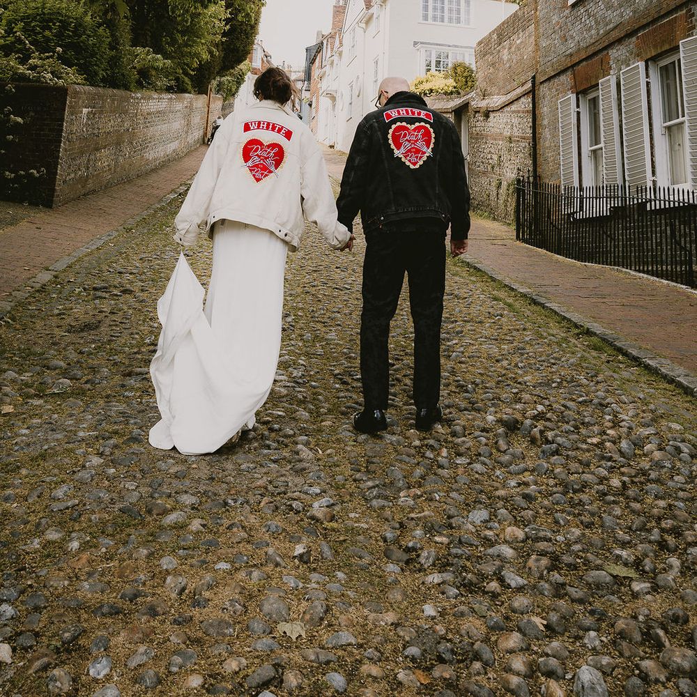 Bride and groom walk hand in hand down a cobbled street wearing matching customised denim jackets