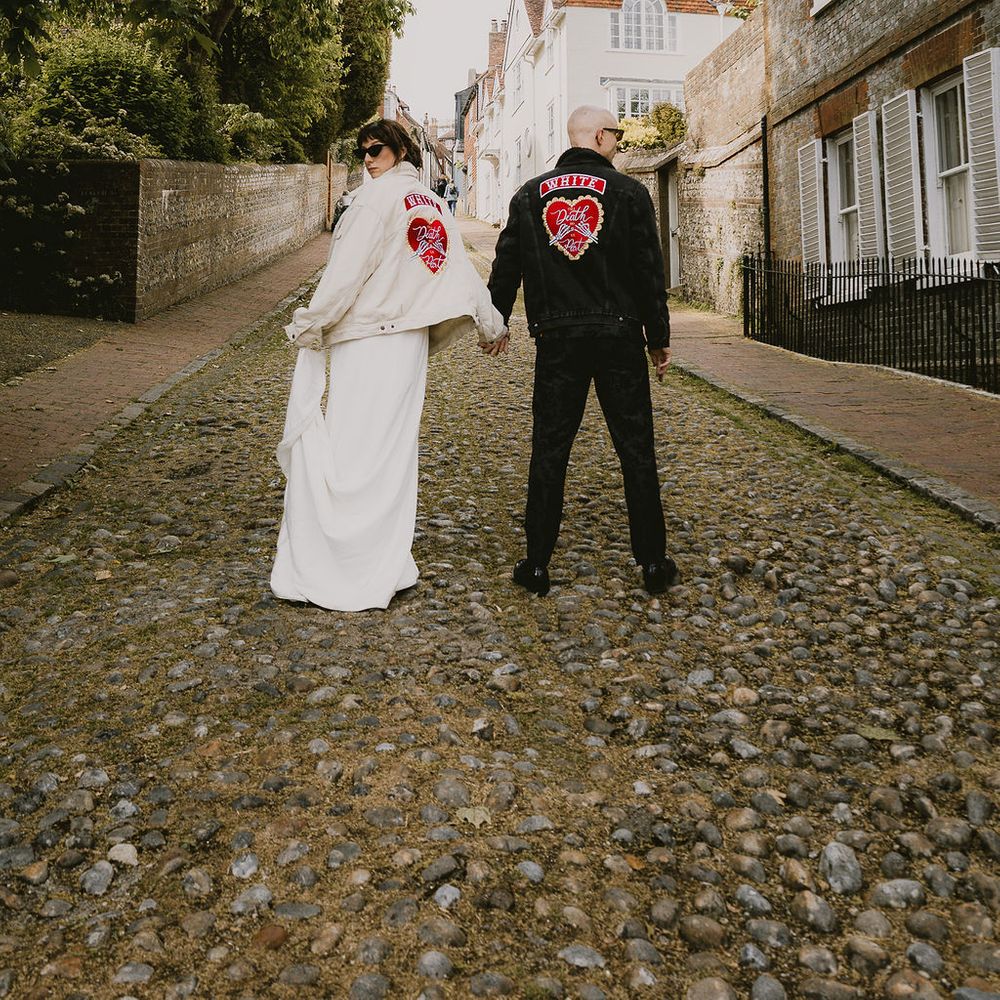 Bride and groom in personalised denim jackets holding hands on a cobbled street