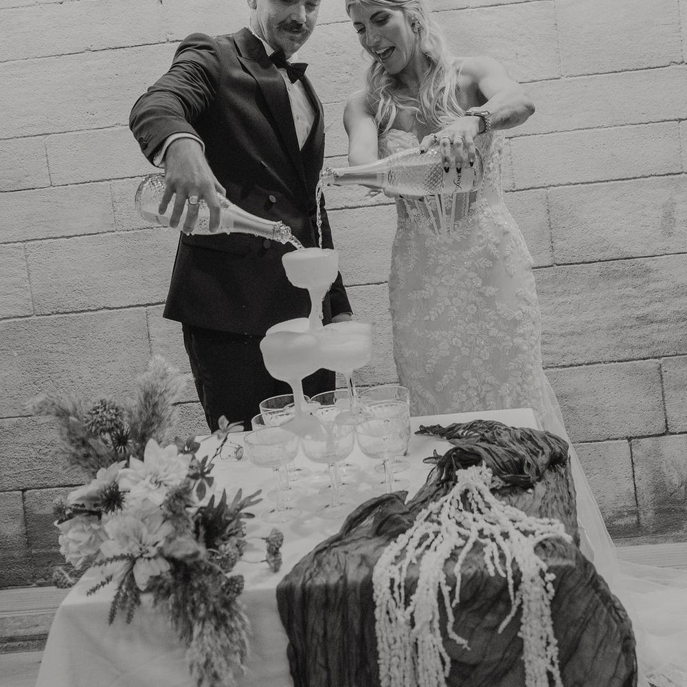 Bride and groom pouring champagne over a coupe tower beneath a personalised neon sign