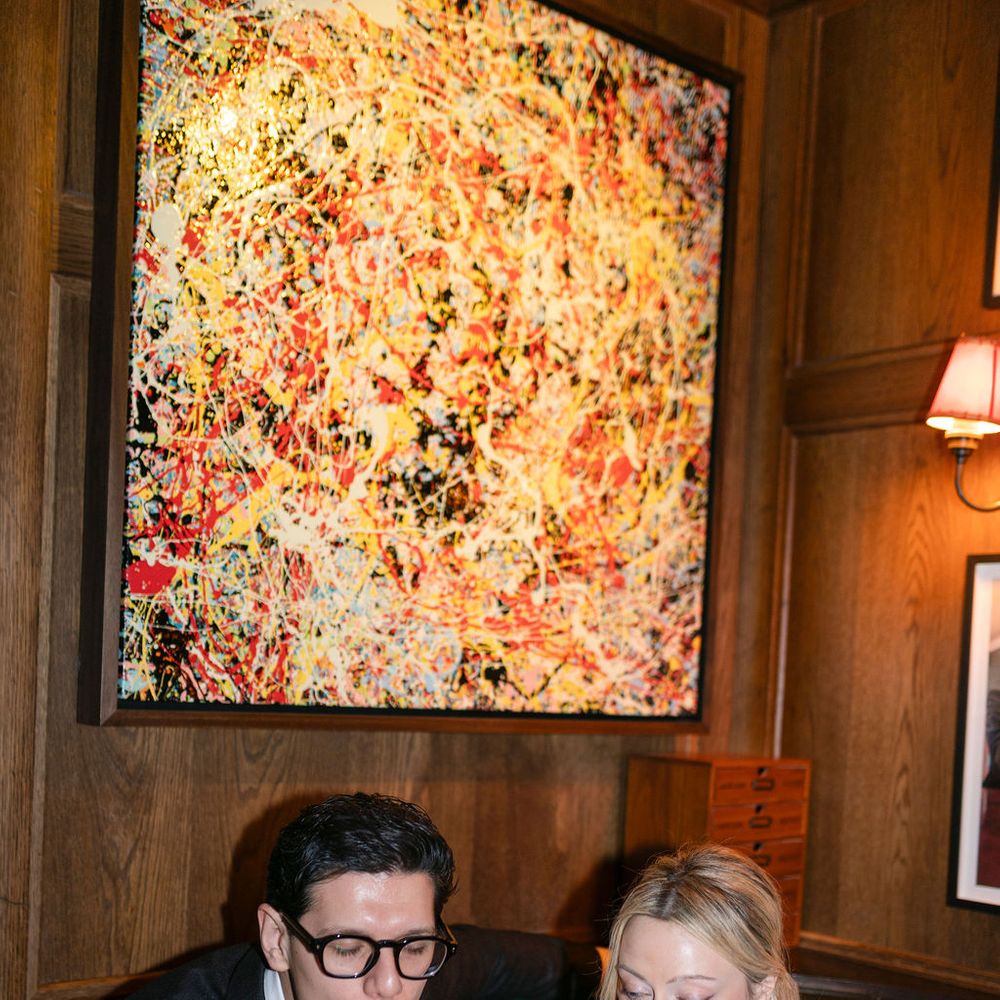 Couple sipping pints of Guinness on a green leather banquette beneath abstract art