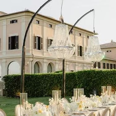 Outdoor reception table with crystal chandeliers suspended before a grand pastel villa