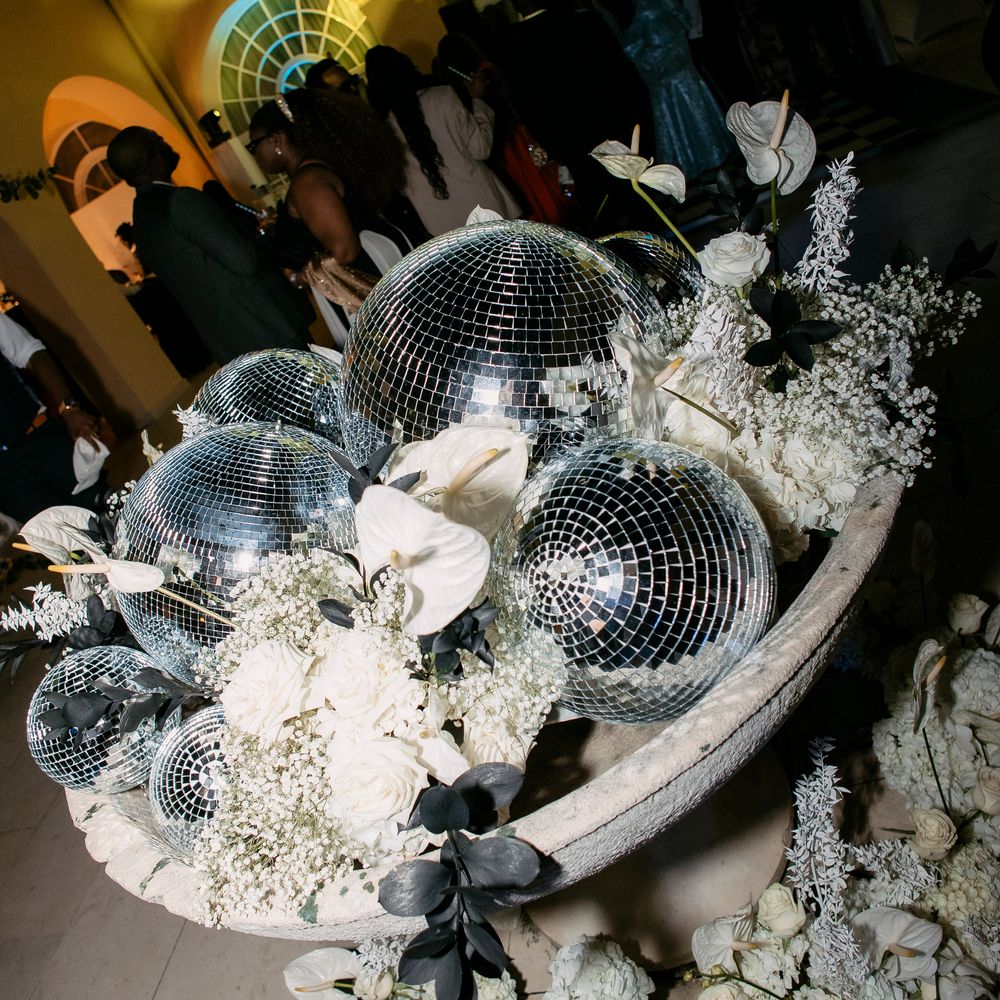 Stone urn filled with disco balls, white anthuriums and roses at an evening reception