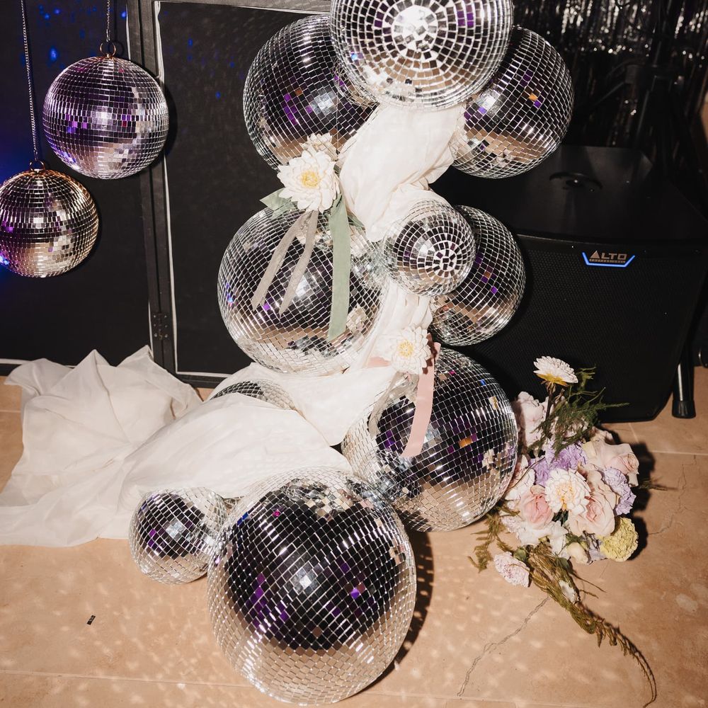 Cluster of mirrored disco balls with white drapery and pastel florals against a shimmering silver backdrop