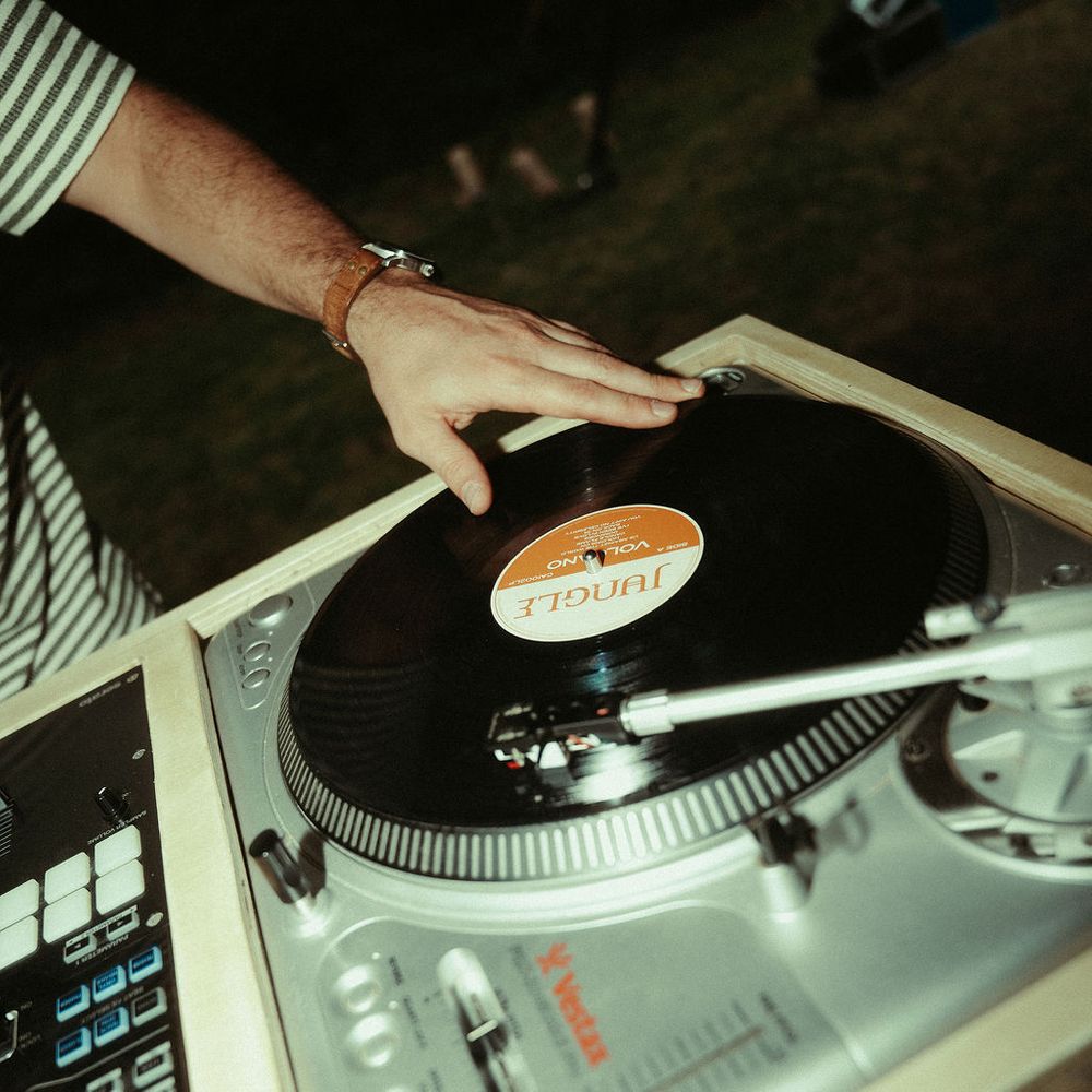 DJ's hand resting on a vinyl record spinning on a turntable at an outdoor evening reception