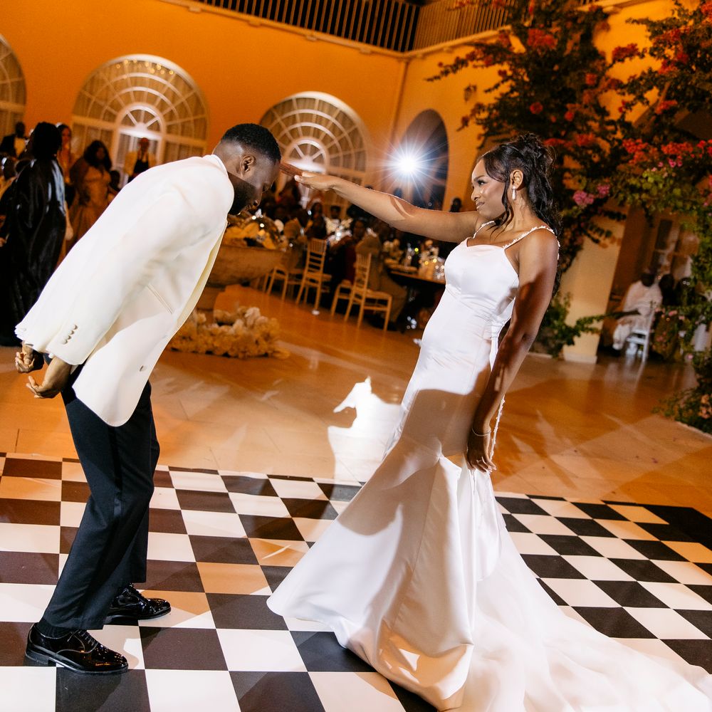 Bride and groom dancing on a black and white chequered floor beneath festoon lights at night