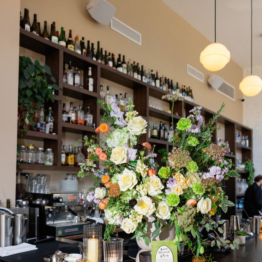Lush floral arrangement of roses, sweet peas and greenery on a bar with candles and signage