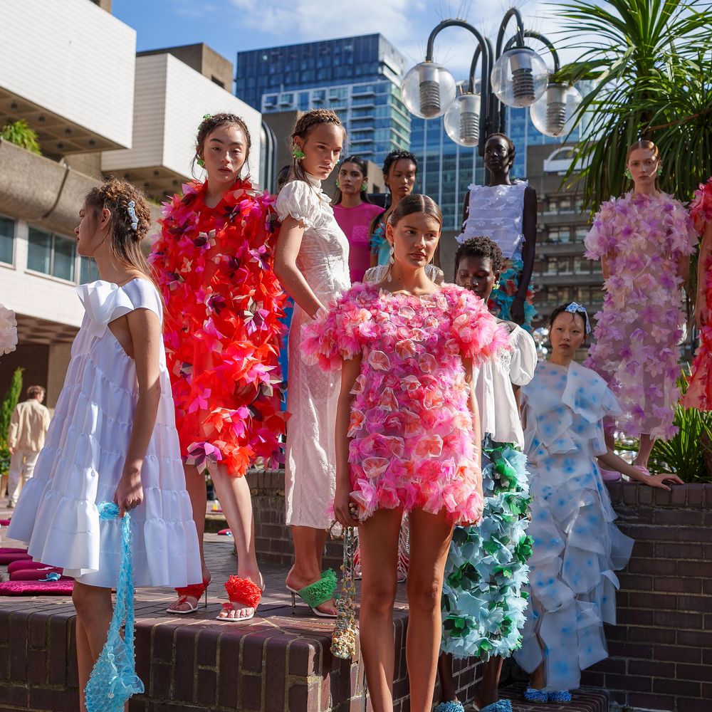 Models in textured floral and pastel dresses posed on brick steps at an outdoor city fashion show