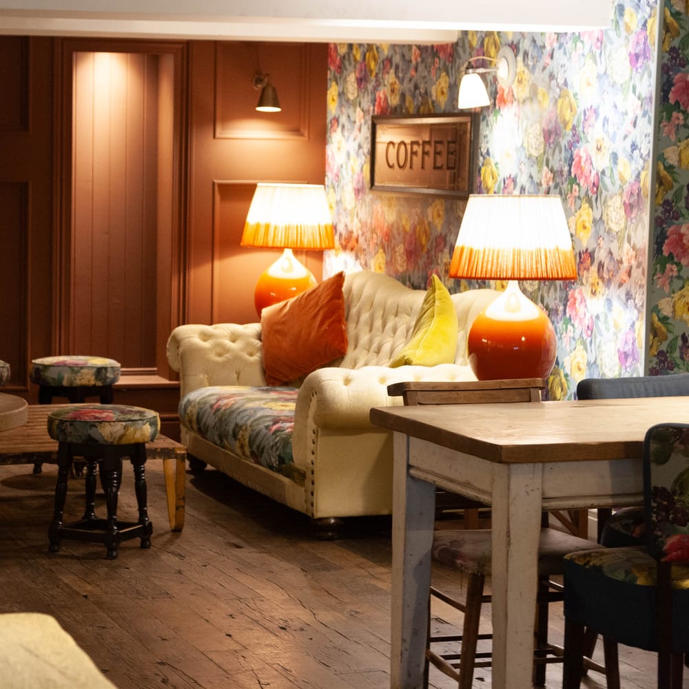 Cosy lounge with a cream Chesterfield sofa, floral wallpaper and warm lamplight
