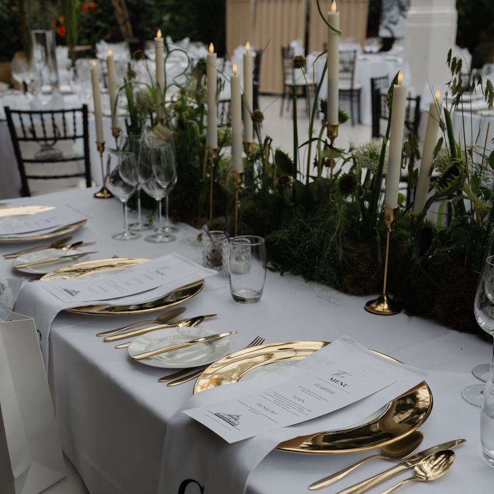 Elegant wedding table setting with gold chargers, cutlery, taper candles and monogrammed napkins