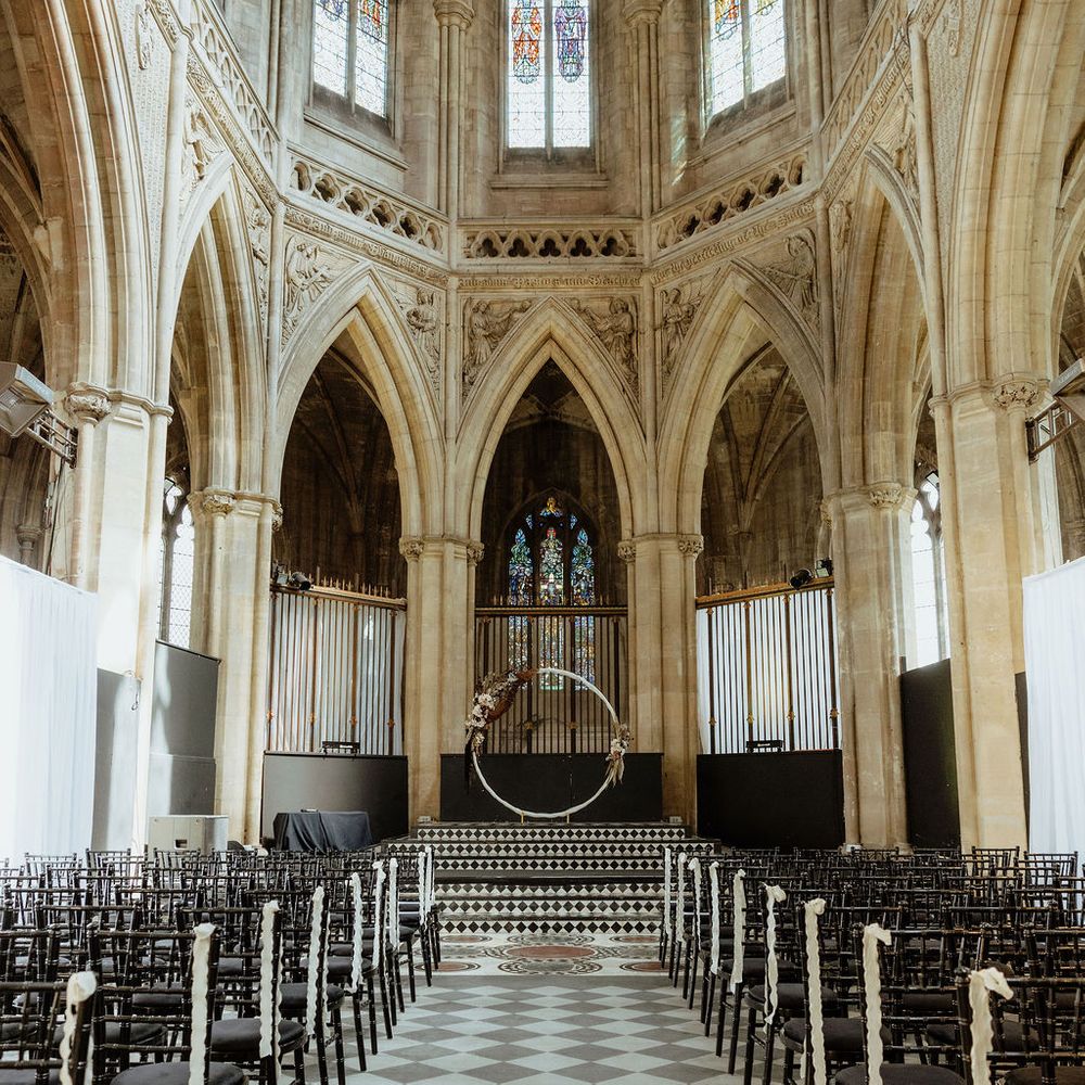 Gothic chapel ceremony aisle with checkerboard floor, black chairs and a floral moon gate altar