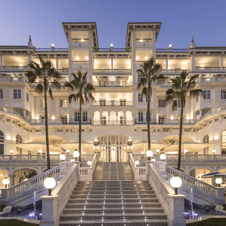 Gran Hotel Miramar Malaga destination wedding hotel illuminated hotel facade at dusk with tiled staircase, palm trees and glowing lanterns