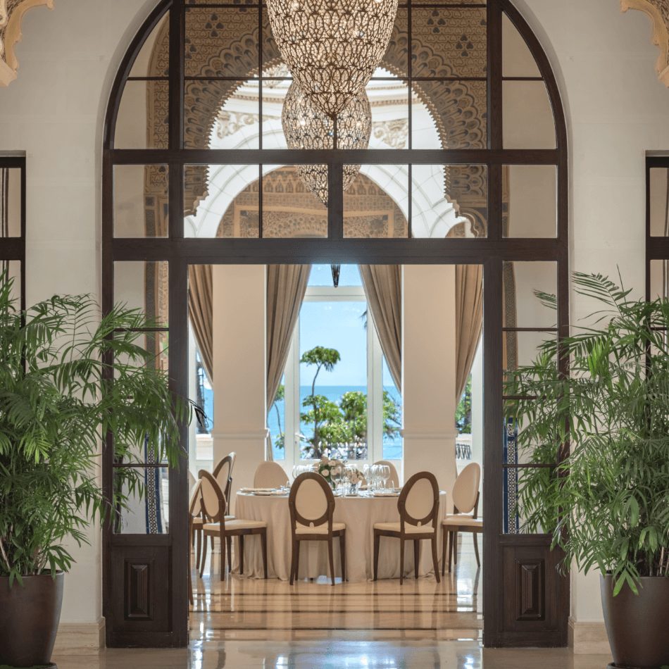 Round dining table set for a meal framed by an arched doorway with ocean views beyond
