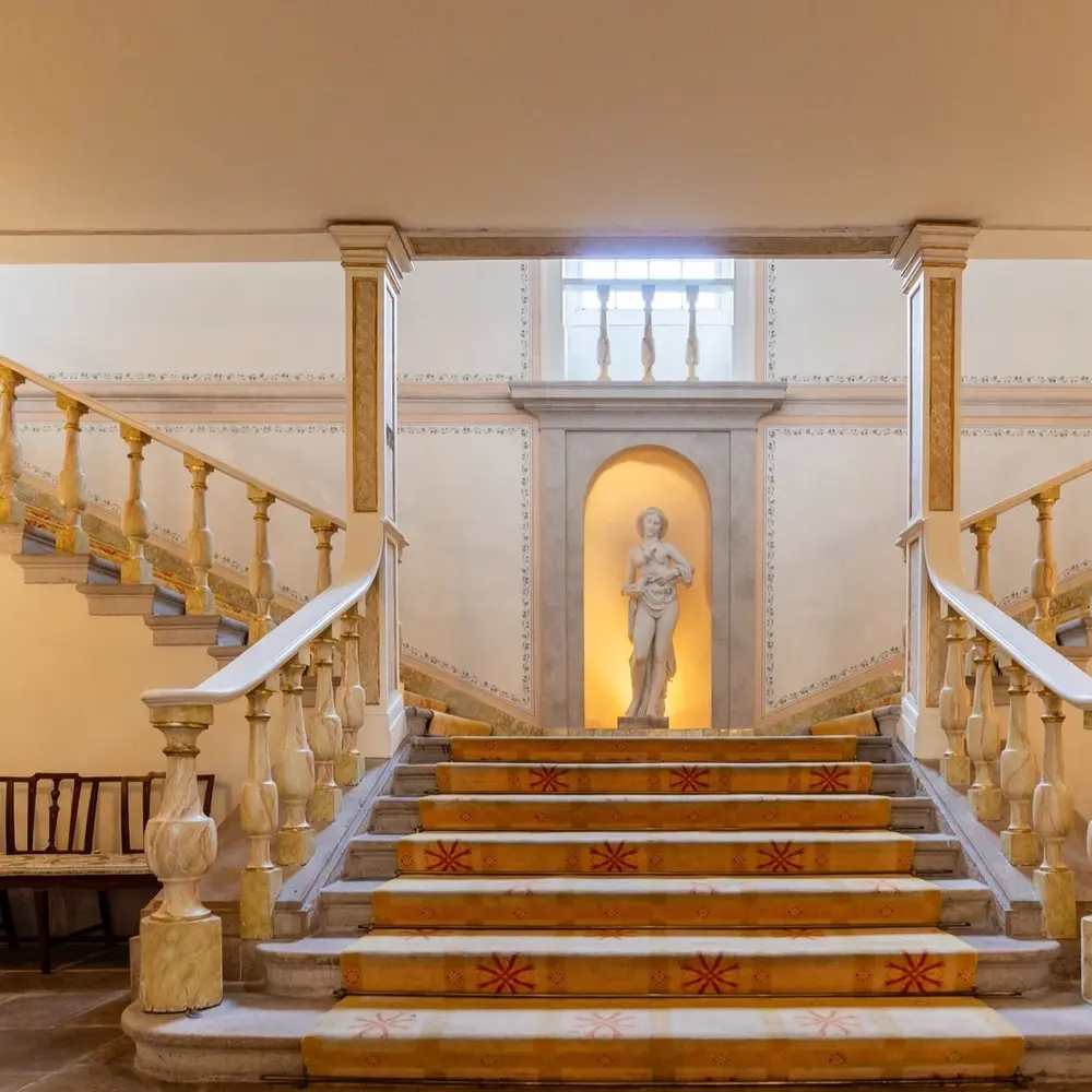 Grand marble staircase with ornate balustrades and a classical statue set in a wall niche.