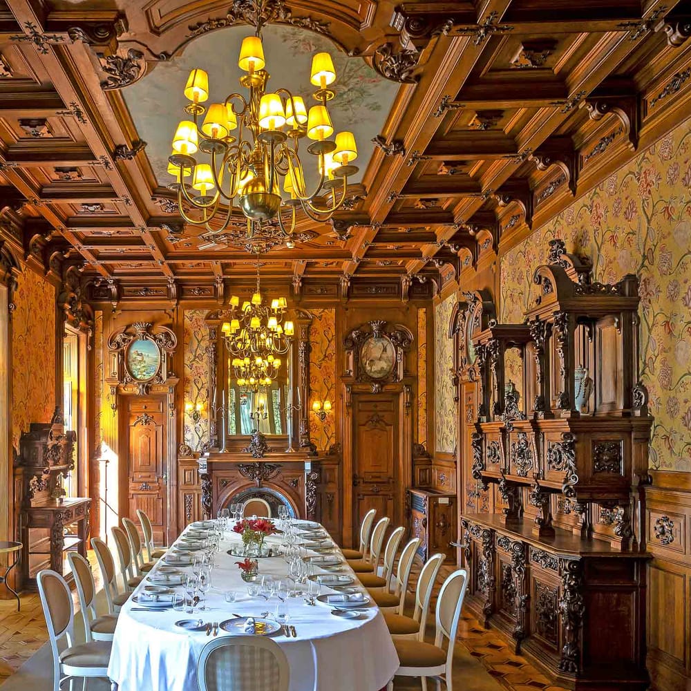 Grand wood-panelled dining room set for a long table with crystal chandeliers and floral wallpaper