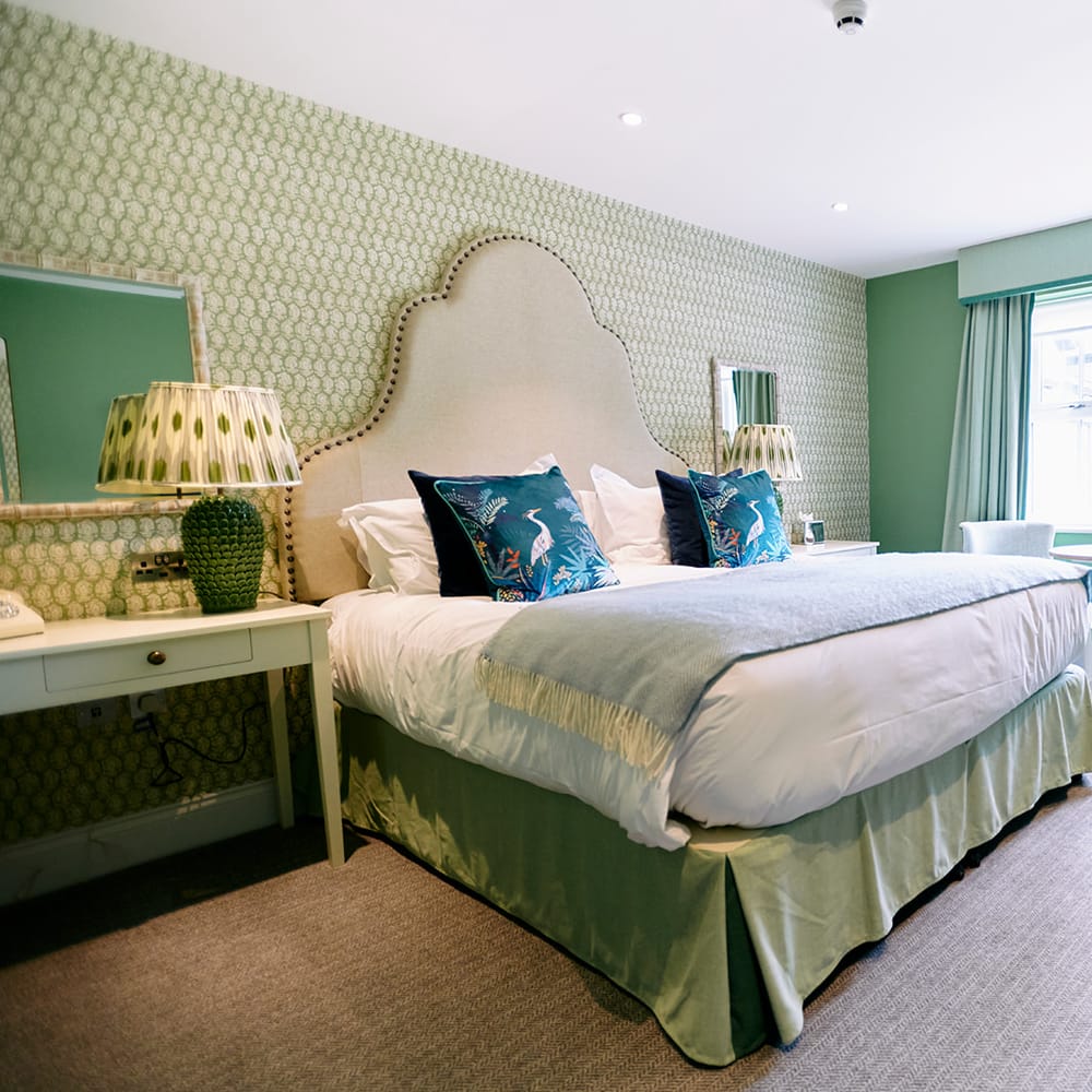 Green-themed bridal suite with upholstered headboard, patterned wallpaper and seating by a bay window