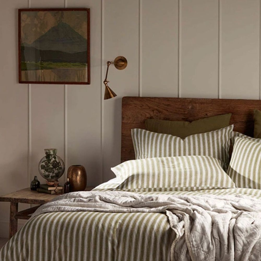 Rustic bedroom with green striped linen bedding, wooden headboard and brass wall light