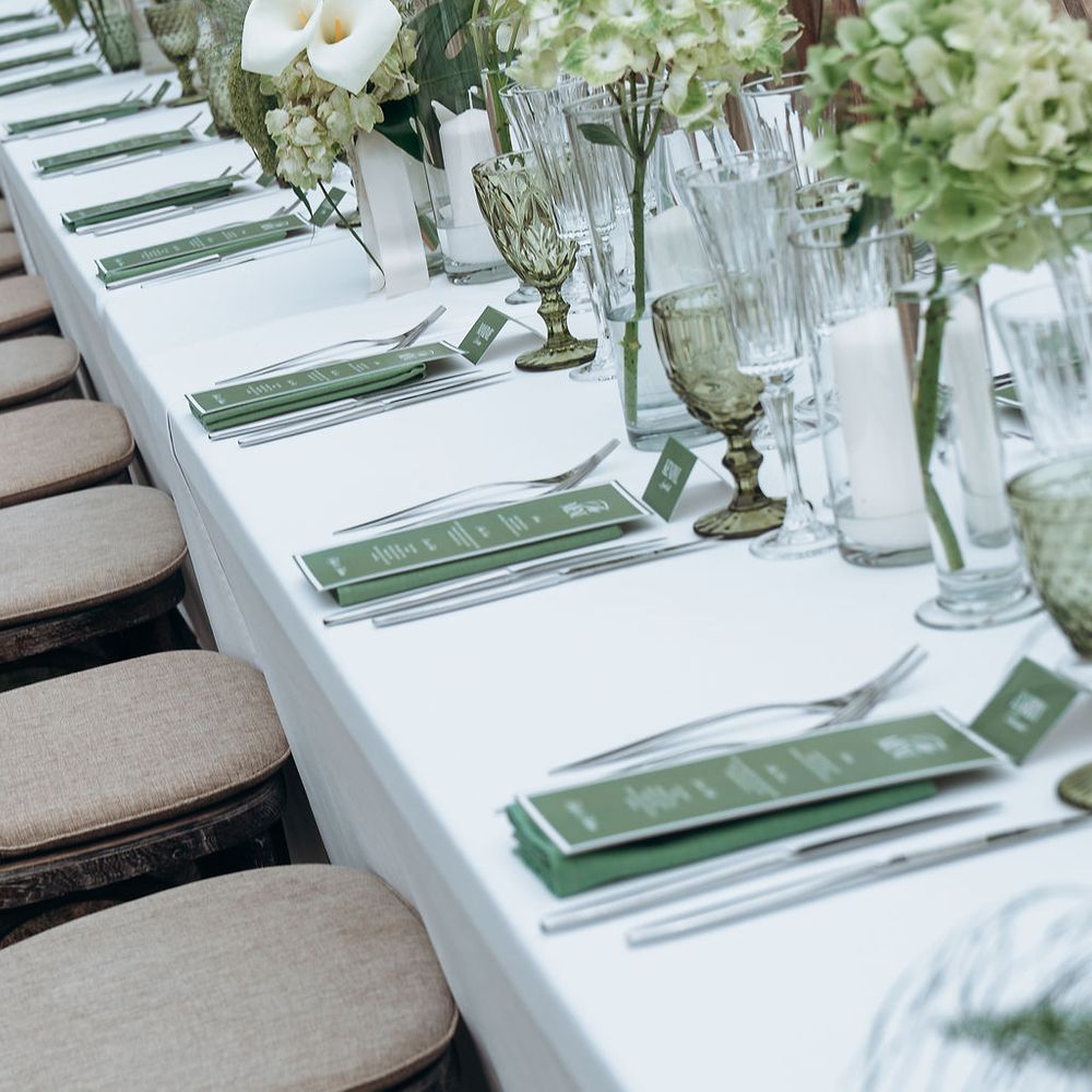 Long white table set with green menus, hydrangeas and coloured glassware alongside linen chairs