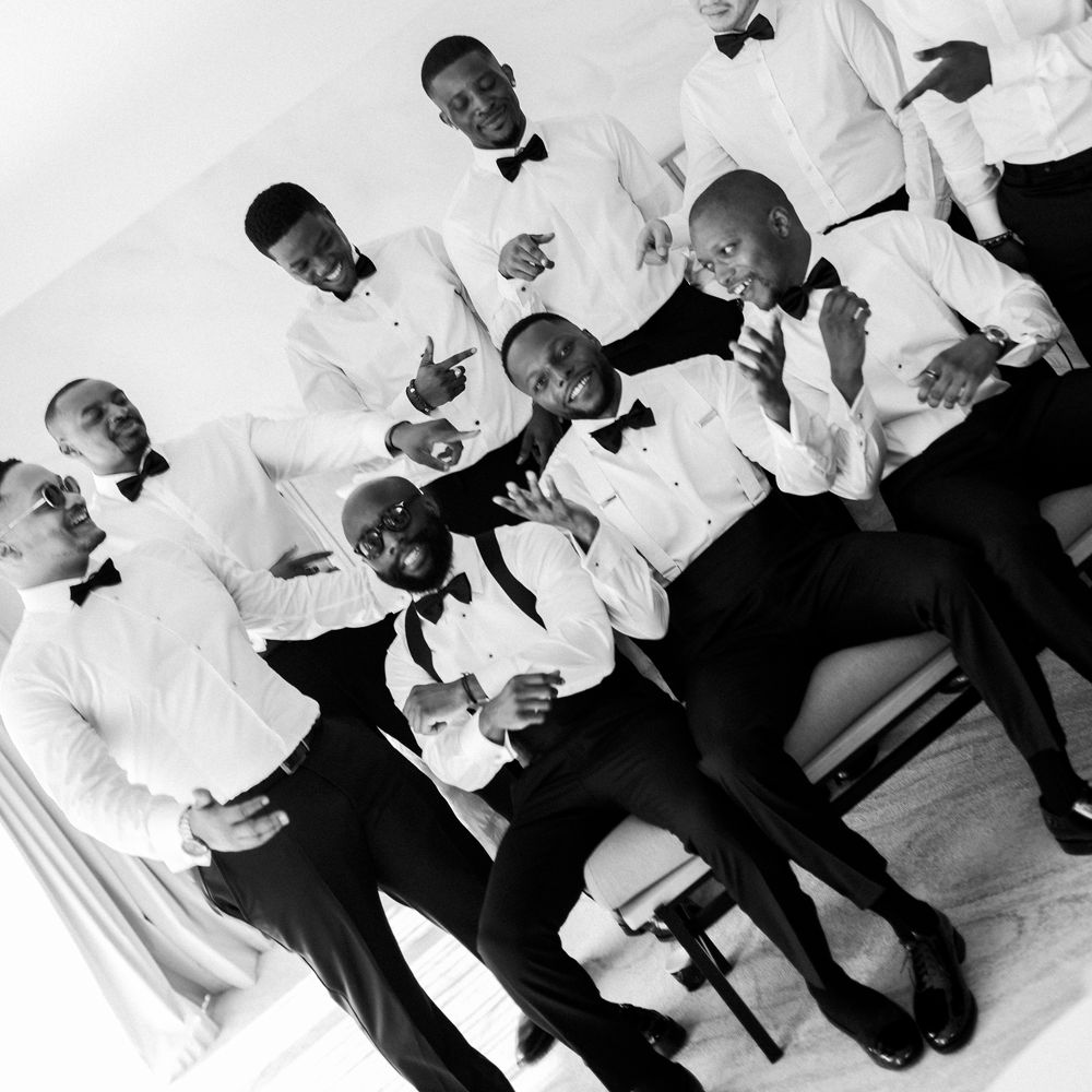 Groom and groomsmen in black bow ties laughing together in a bright room