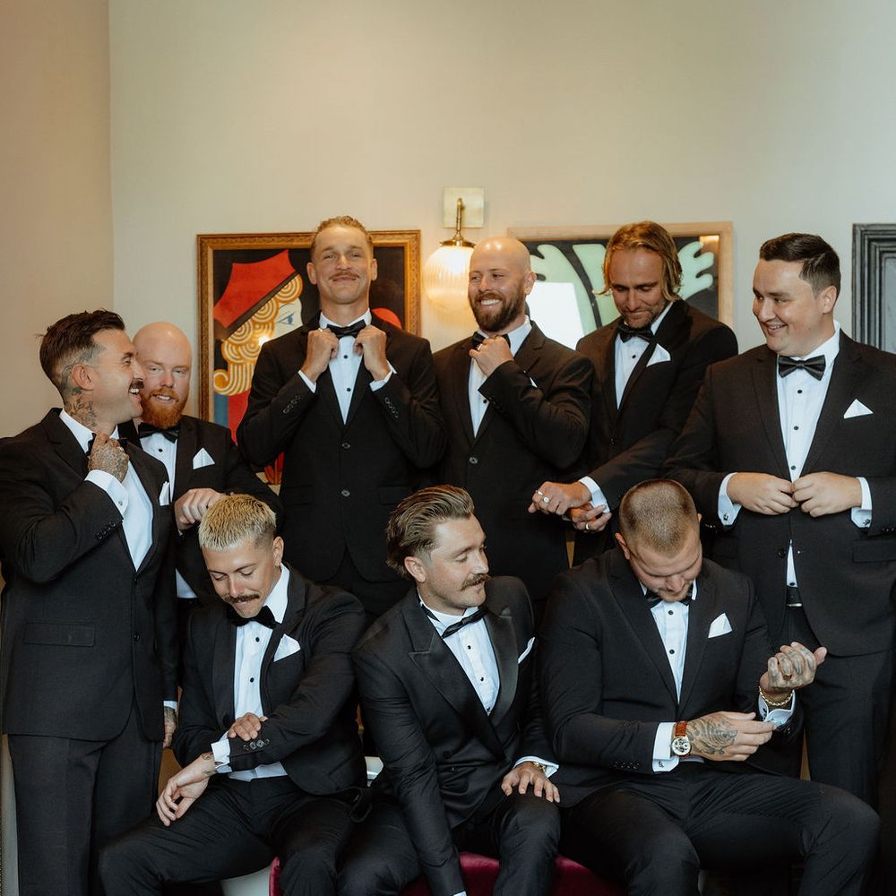 Groom and groomsmen in black tuxedos and bow ties adjusting attire in a stylish room