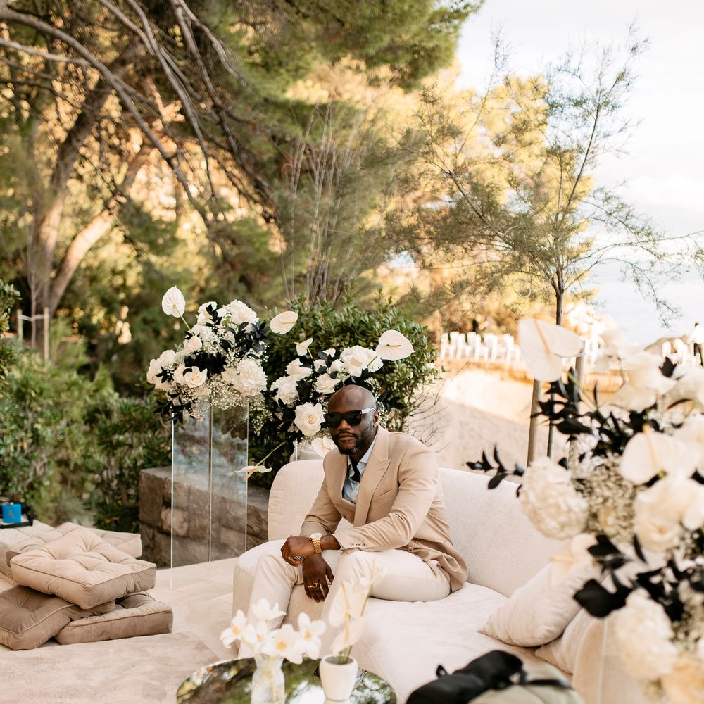 Groom in tan suit and sunglasses relaxes on cream sofa in an outdoor lounge setting