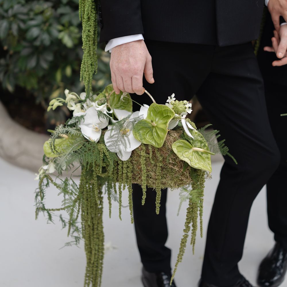 Groom in black tuxedo holding a trailing green and white bouquet with anthurium and amaranthus