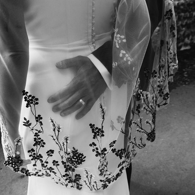 Groom's hand resting on bride's waist over floral embroidered gown with wedding ring visible