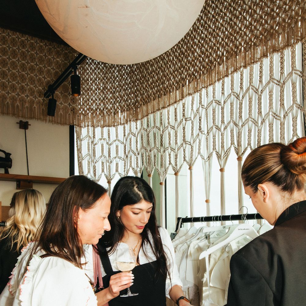 Guests browse a lookbook beside a rail of bridal gowns in a macramé-styled room