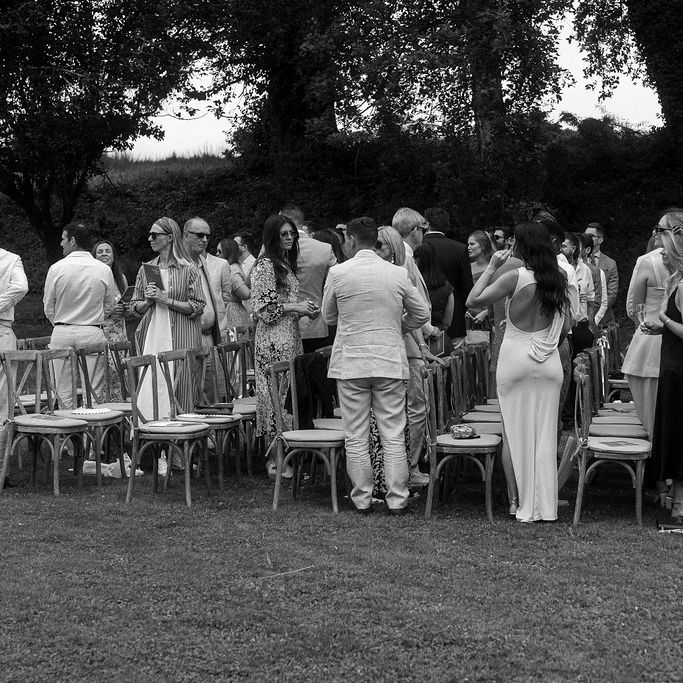 Guests in summer attire mingling among wooden chairs at an outdoor garden ceremony
