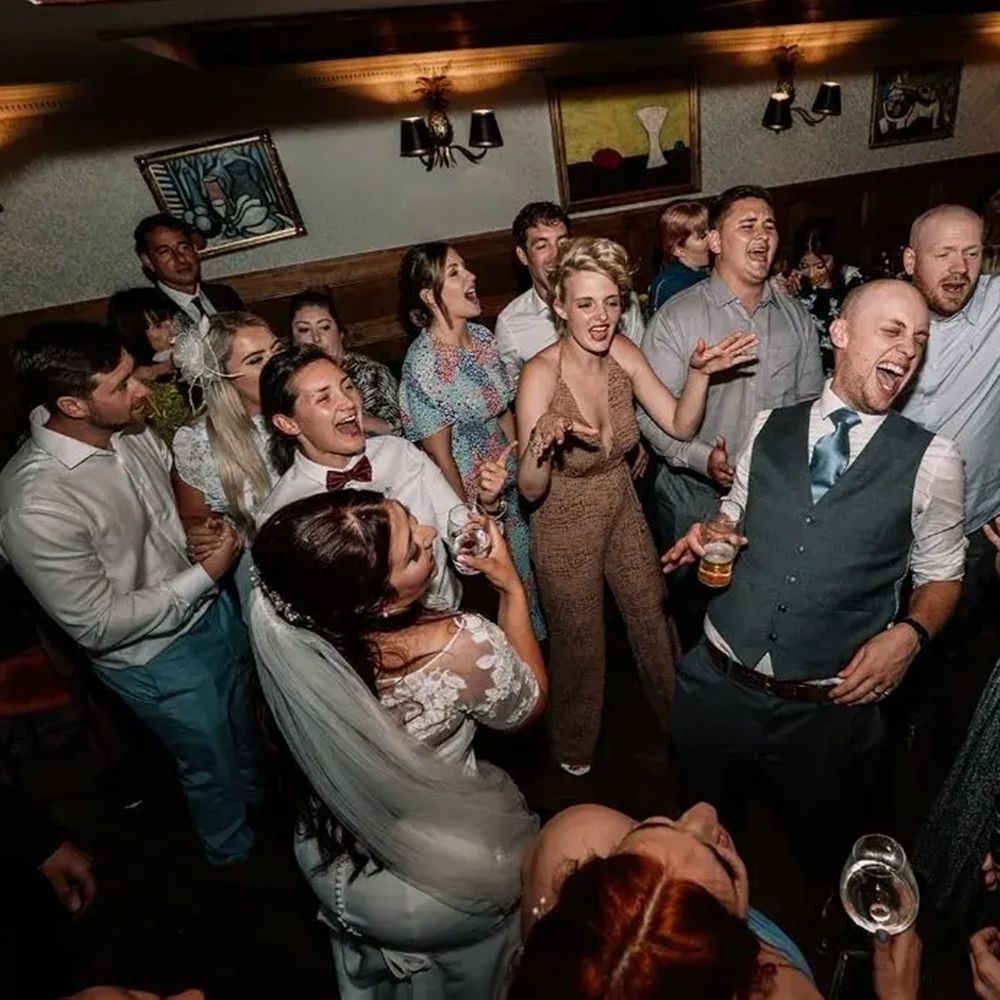 Guests and newlyweds singing and dancing together on a lively evening reception dance floor