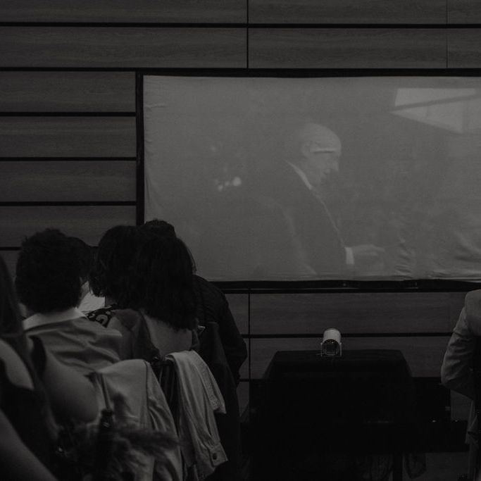 Guests watch a projected film screening on a large screen in a dimly lit room