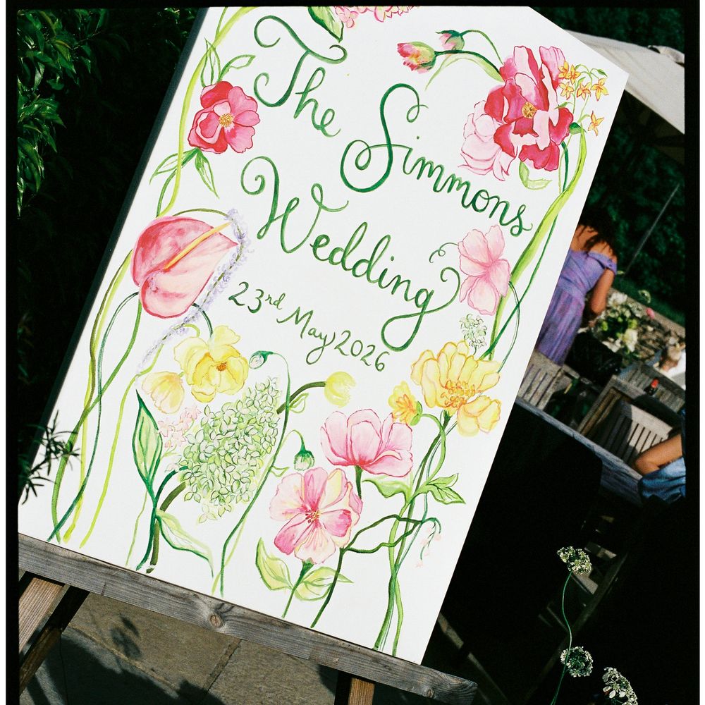 Hand-painted floral watercolour wedding welcome sign on a wooden easel beside fresh blooms