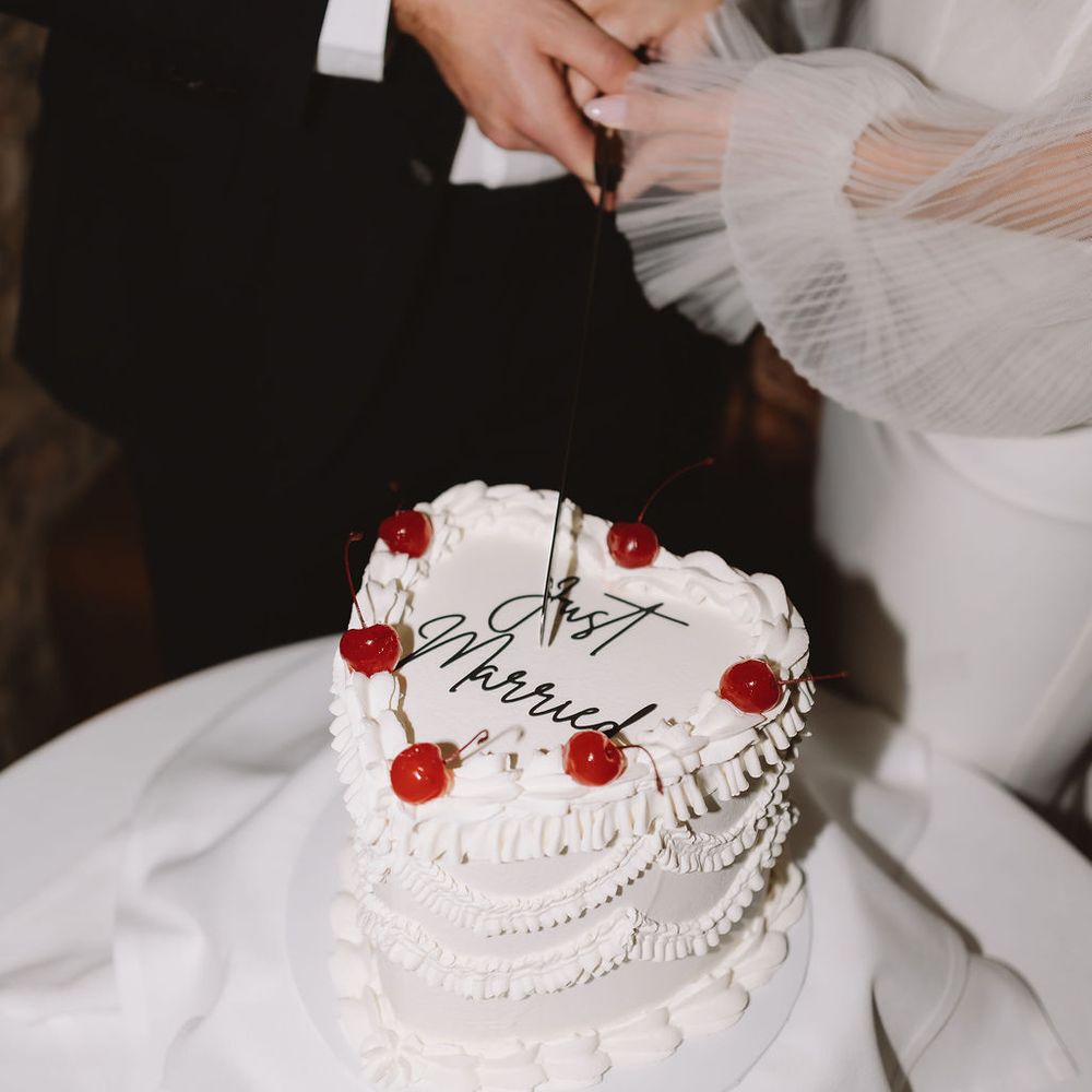 Couple cutting a white heart-shaped cake topped with cherries and 'Just Married' piping