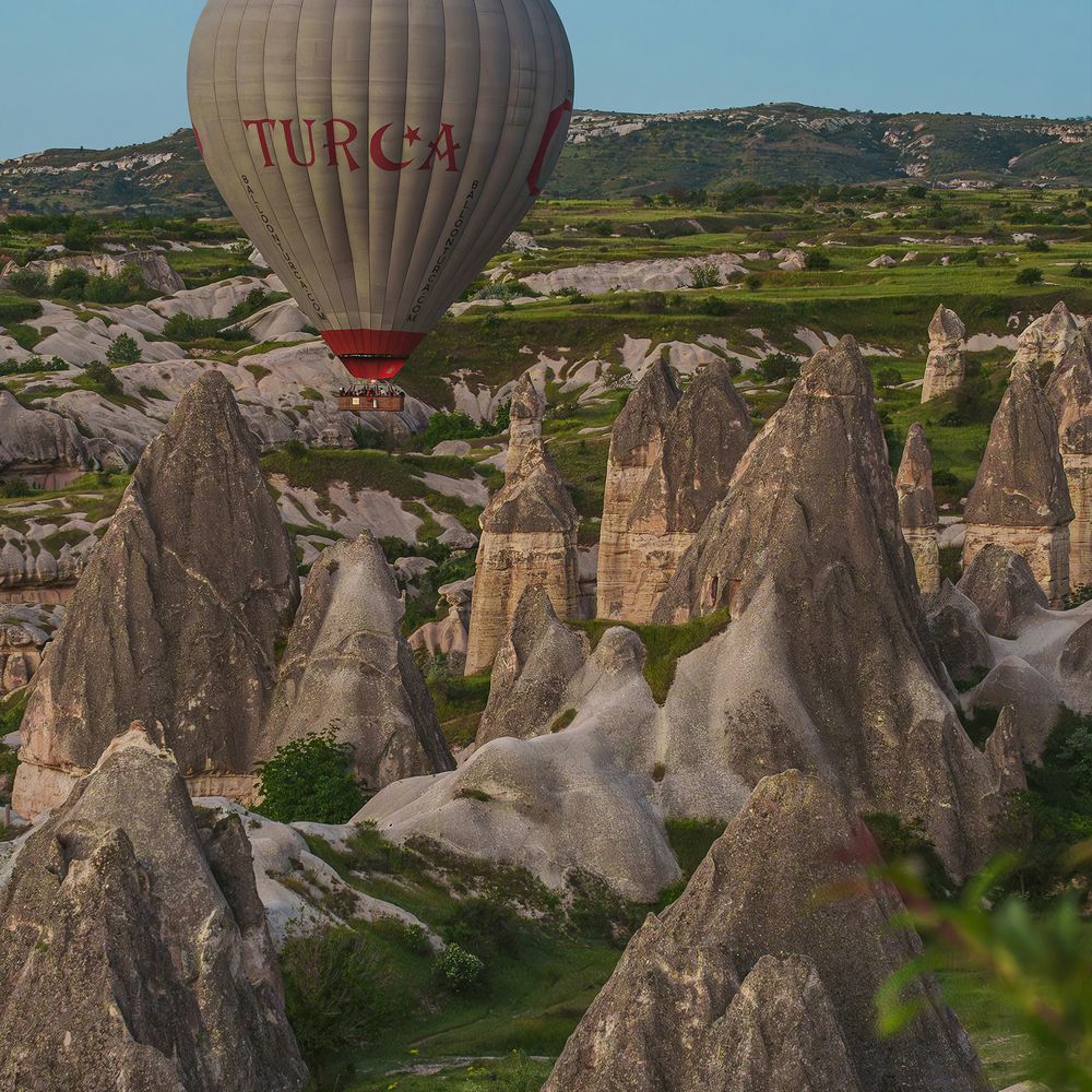 Hot air balloon drifting above dramatic rock formations in a valley at dawn