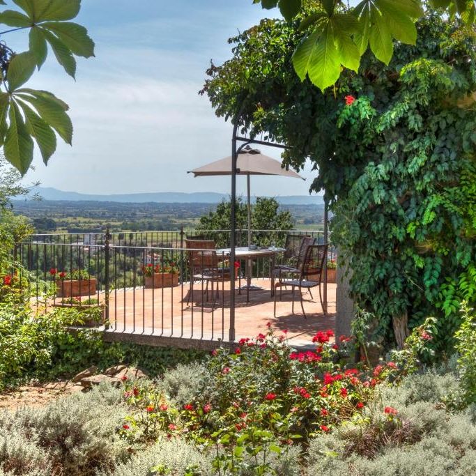 Stone farmhouse terrace with parasol and dining set overlooking a countryside valley in bloom