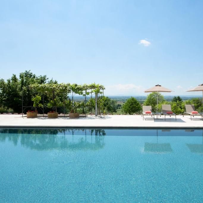 Poolside sun loungers and parasols overlooking rolling countryside under a clear blue sky