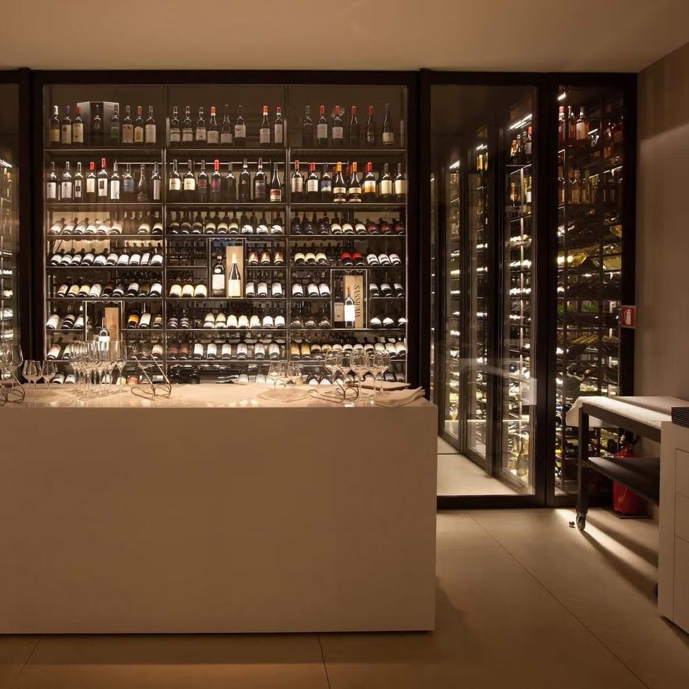 Illuminated wine cellar with backlit bottle displays and a central tasting table set with glasses.