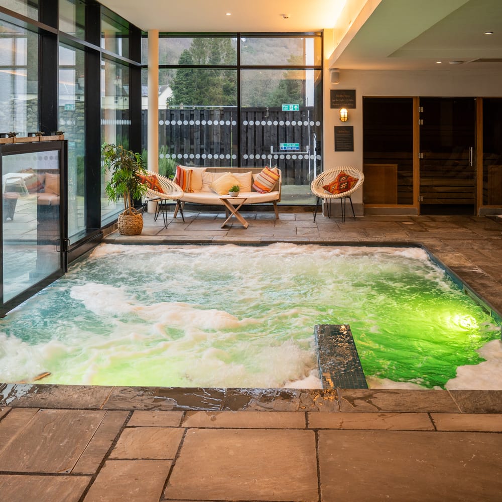 Indoor spa hydrotherapy pool with bubbling water and green lighting beside glass doors and a seating area