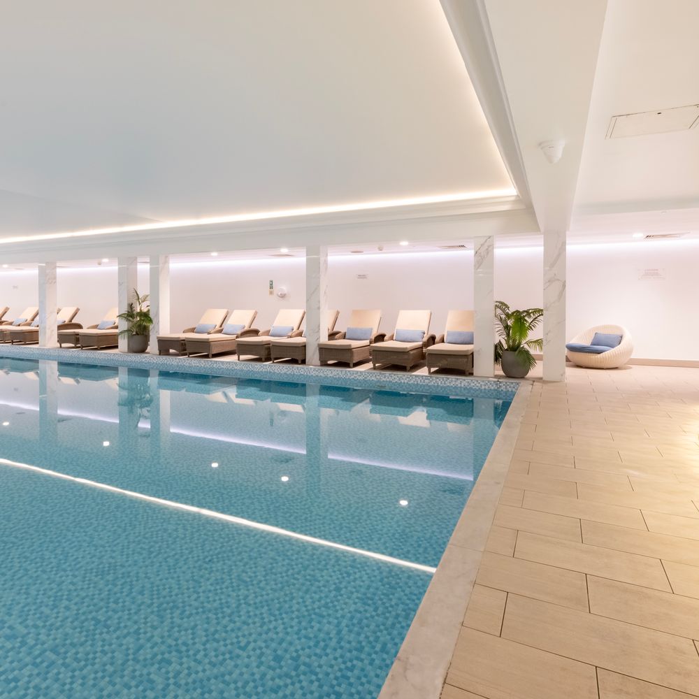 Indoor spa swimming pool lined with rattan sun loungers and marble columns