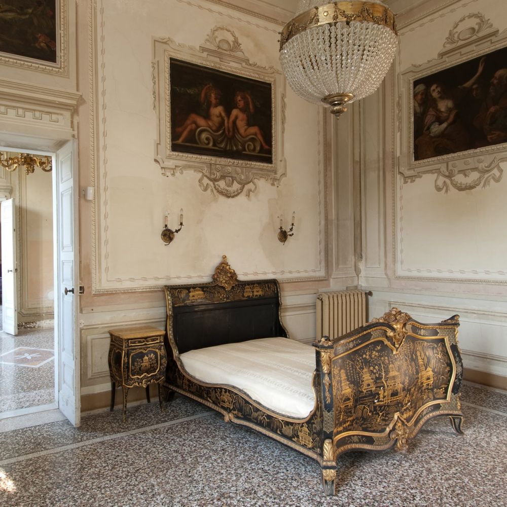 Ornate gilded chinoiserie daybed in a frescoed palazzo room with crystal chandelier