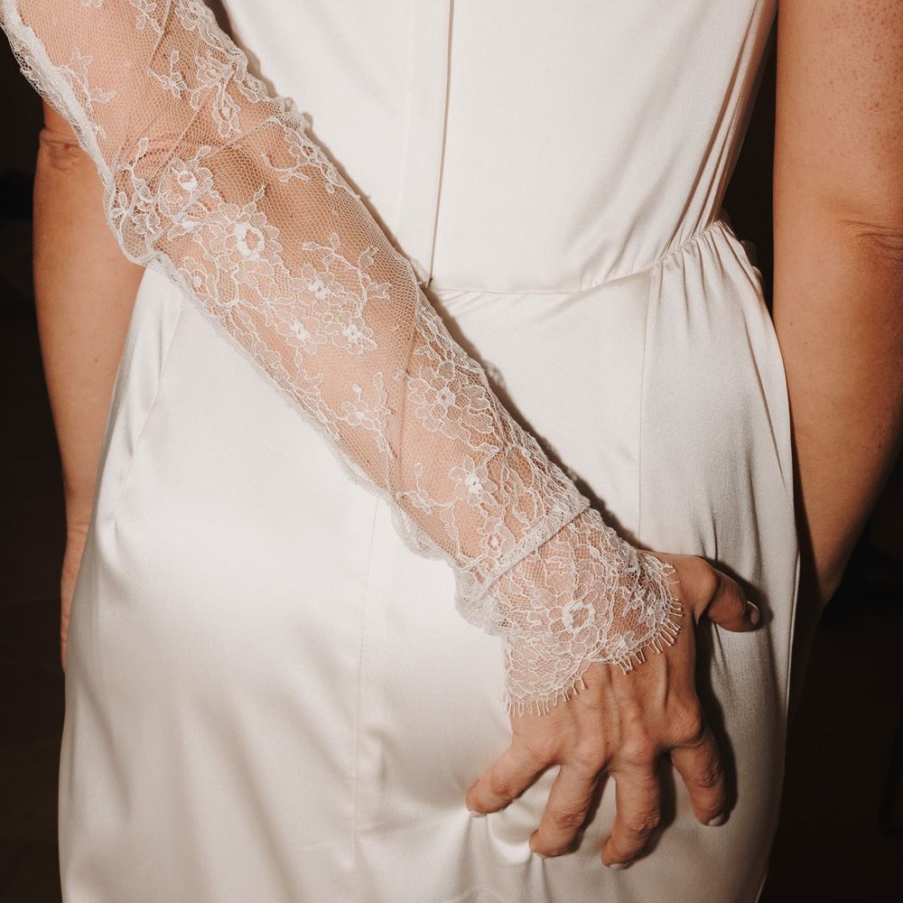 Bride in ivory silk gown wearing a delicate floral lace glove reaching to her waist