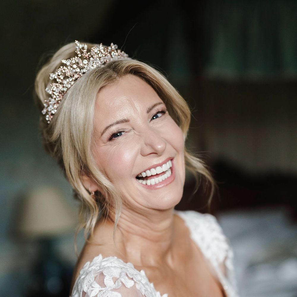 Smiling bride in a floral lace gown wearing a sparkling crystal tiara