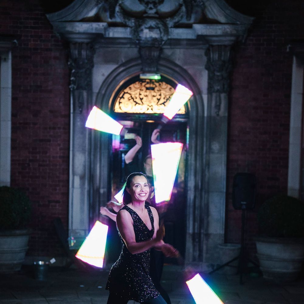 Performer in a black sequinned outfit juggling glowing LED wands outside a lit stone doorway at night