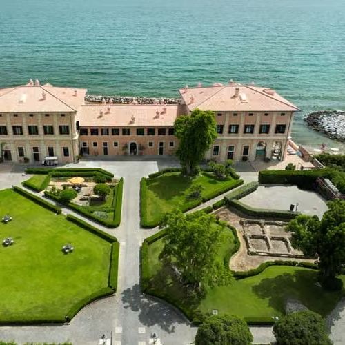 Aerial view of a coastal Italian villa with manicured gardens beside a turquoise sea.